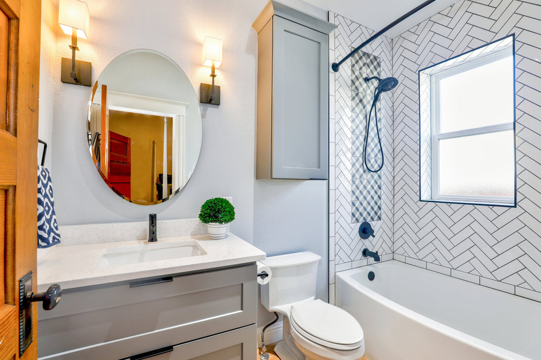 Eine weiße Badezimmer mit zwei Lampen, marmor Waschbecken, Toilette und Badewanne sowie ein Fenster.