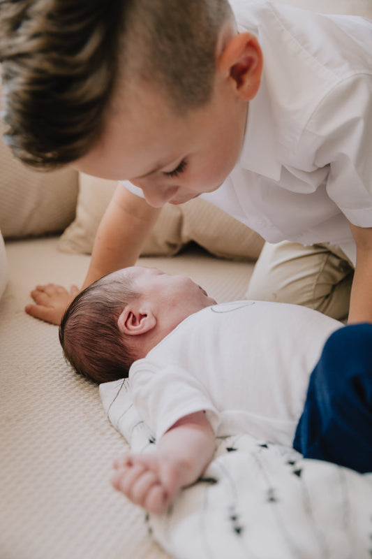 Ein Baby liegt auf einem Sofa und ein Kind stützend aufm Sofa über das Baby mit der Wille das Baby zu küssen.