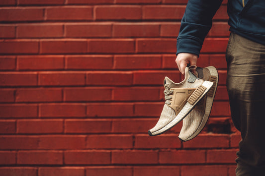 Eine Hand trägt braune Schuhe mit einer orangen Blockwand im Hintergrund.