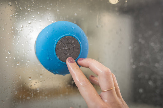 Ein Audiogerät klebt am nassen Glas eines Duschenraums und eine Hand versucht auf Starten-Button zu klicken